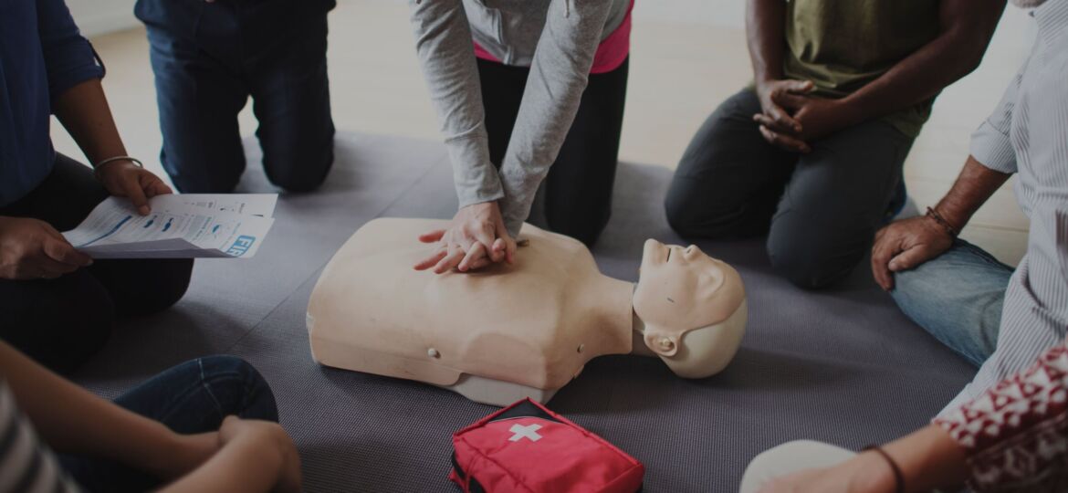 Group of people surrounding a demonstration of CPR on a dummy.