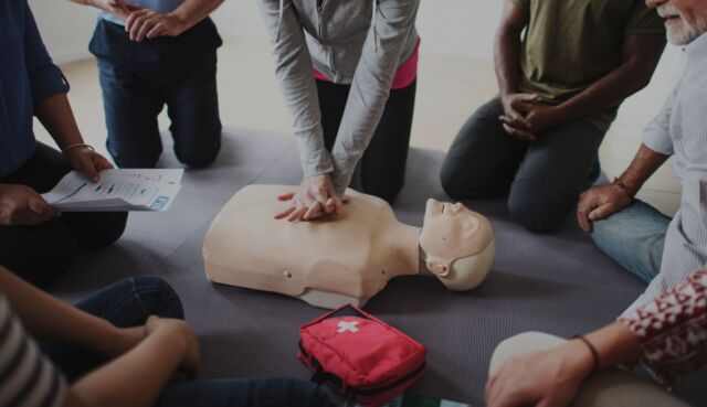 Group of people surrounding a demonstration of CPR on a dummy.